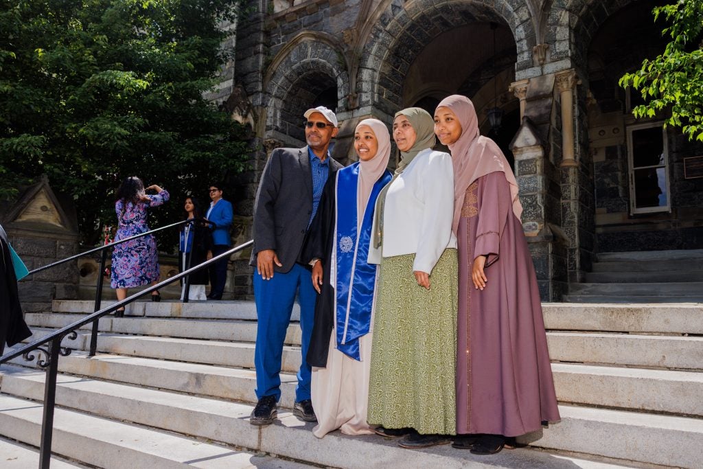A graduate poses with three other people on the steps of Healy Hall during commencement.