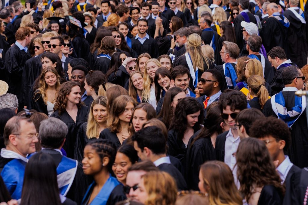 A few graduates look at a camera in a sea of other graduates