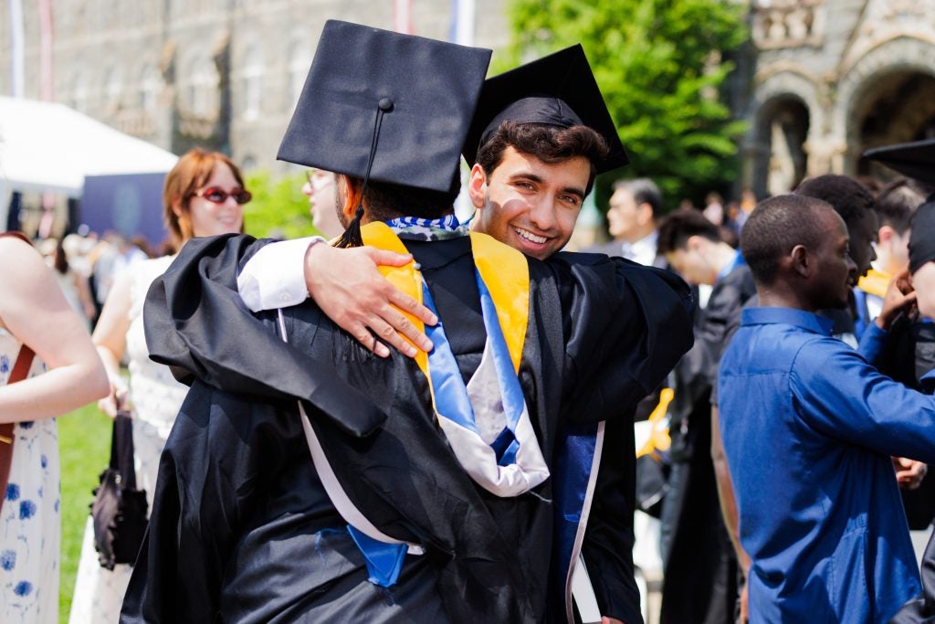 Two young men in graduation robes hug