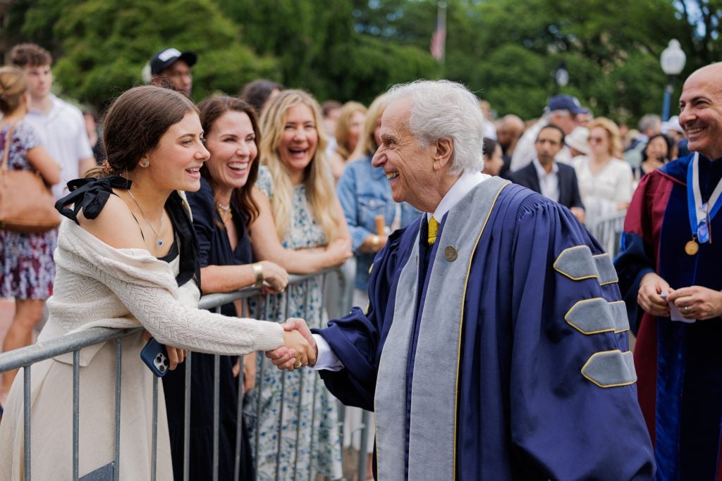 Henry Winkler shakes hands with a woman behind a gate while dressed in a graduation gown