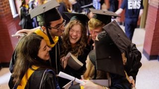 A group of graduates embrace in a hallway