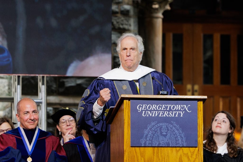 Henry Winkler holds up his fist from behind a podium onstage.