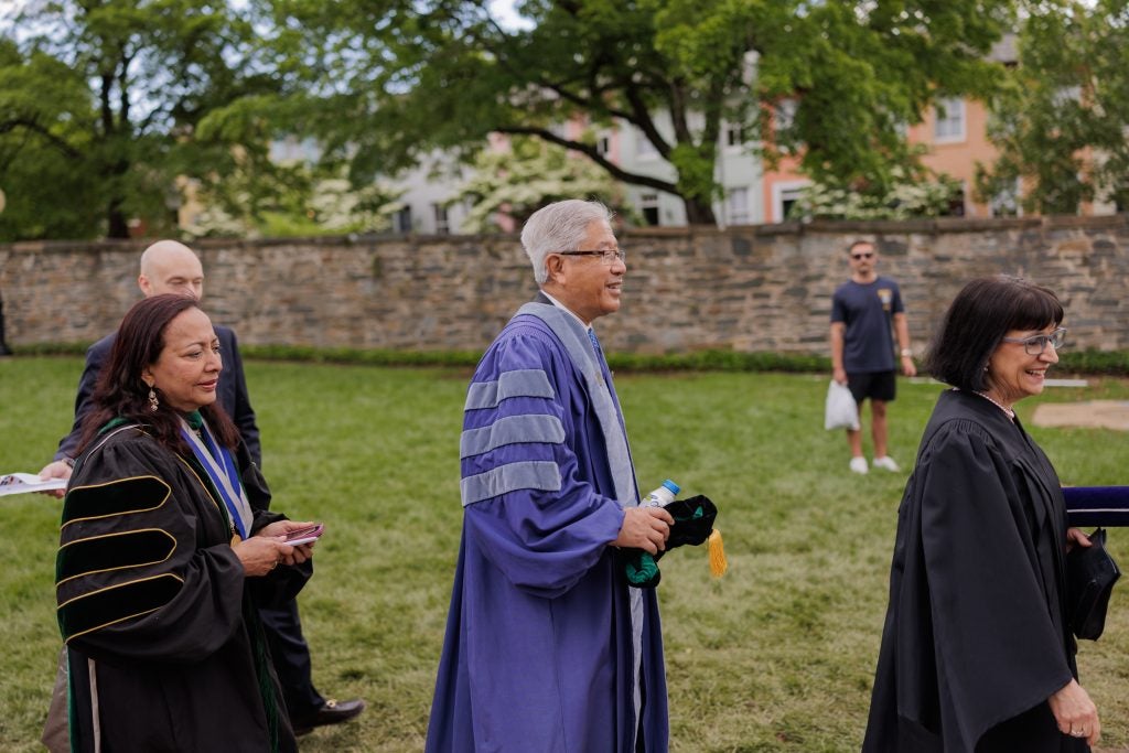 A group of people in graduation gowns process over Georgetown's lawn 