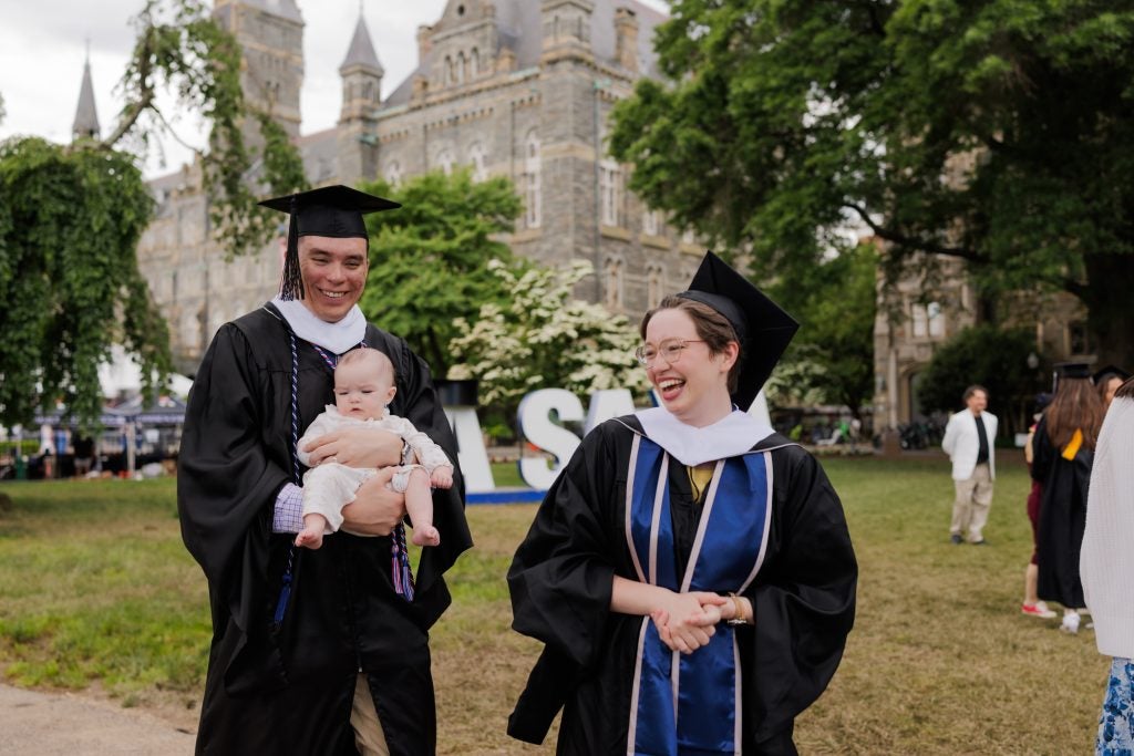 Two graduates with their baby on Healy Lawn