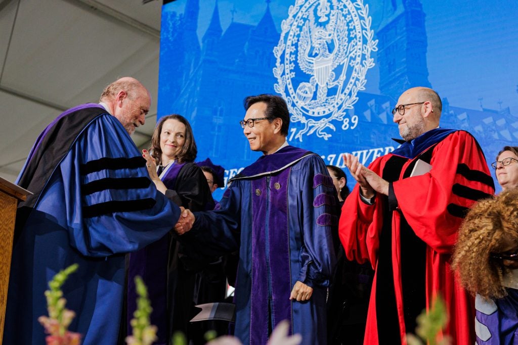 A man in a purple graduation gown greets others onstage