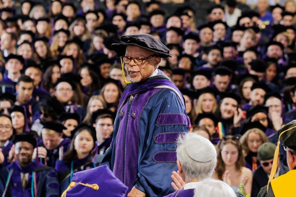 Henry Louis Gates stands before a crowd in a purple and blue graduation gown and a black cap