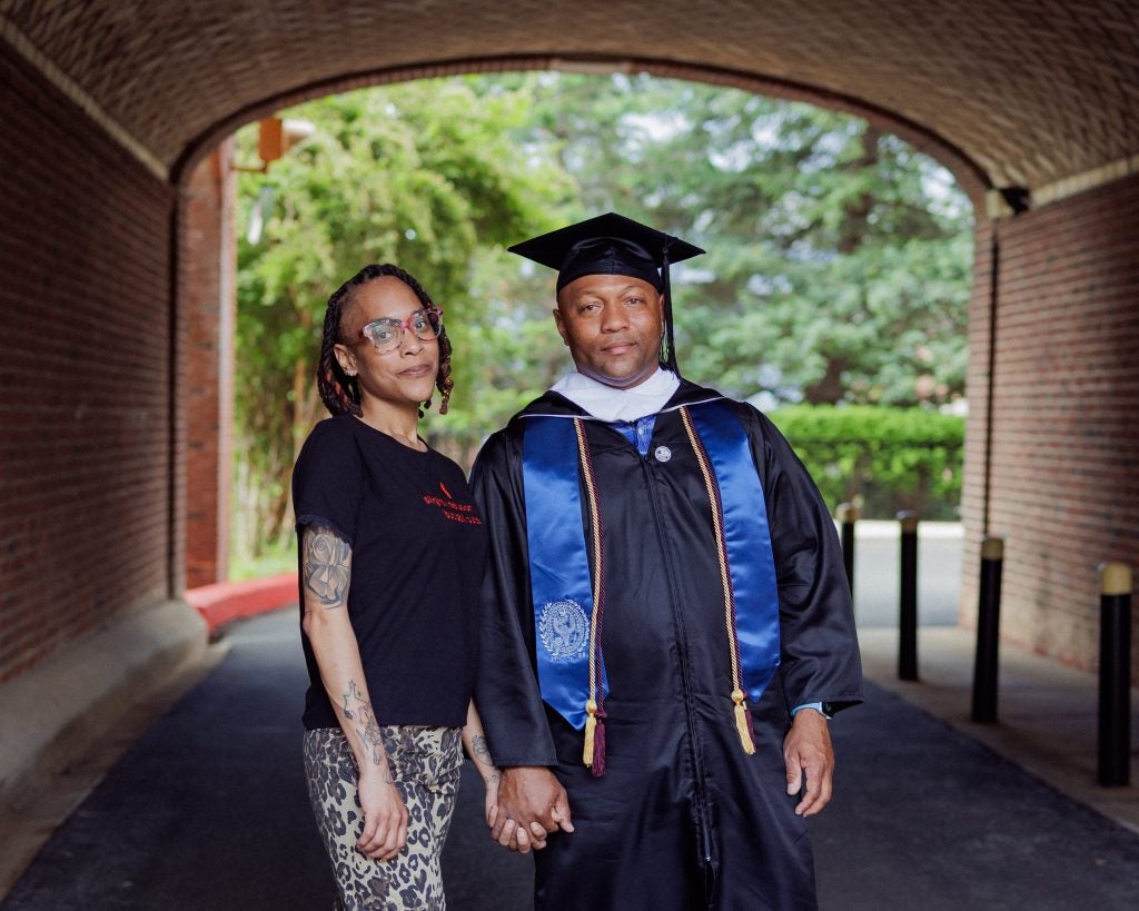 A man in a graduation gown and cap holds hands with his daughter inside a tunnel