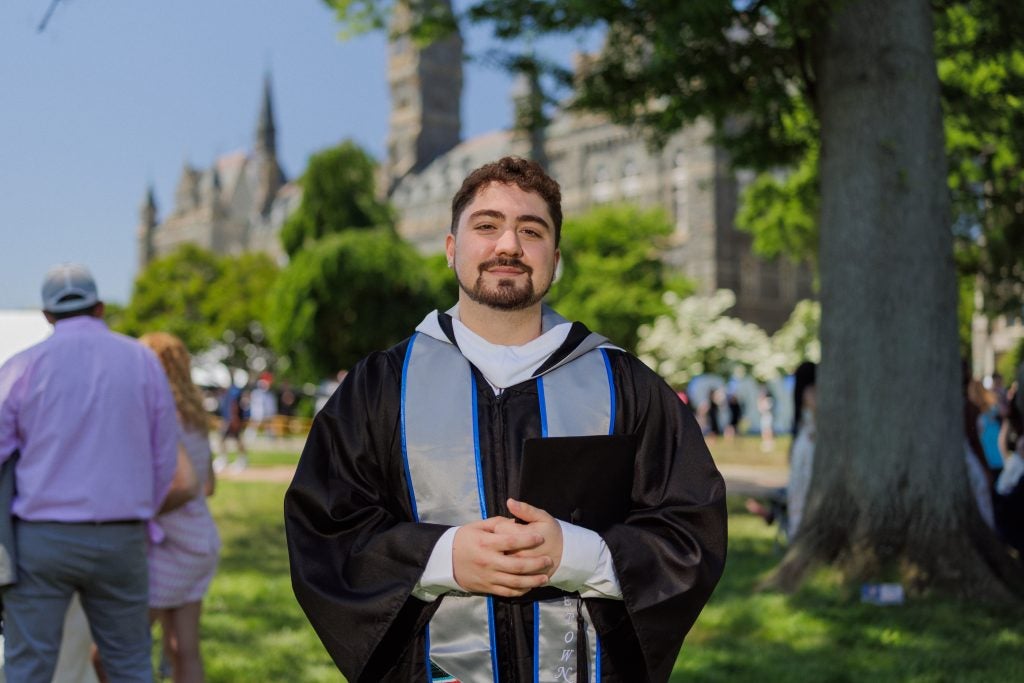 A graduate wears a graduation gown in front of Healy Hall on a sunny day