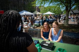 Two young women at a table speak to a young black woman