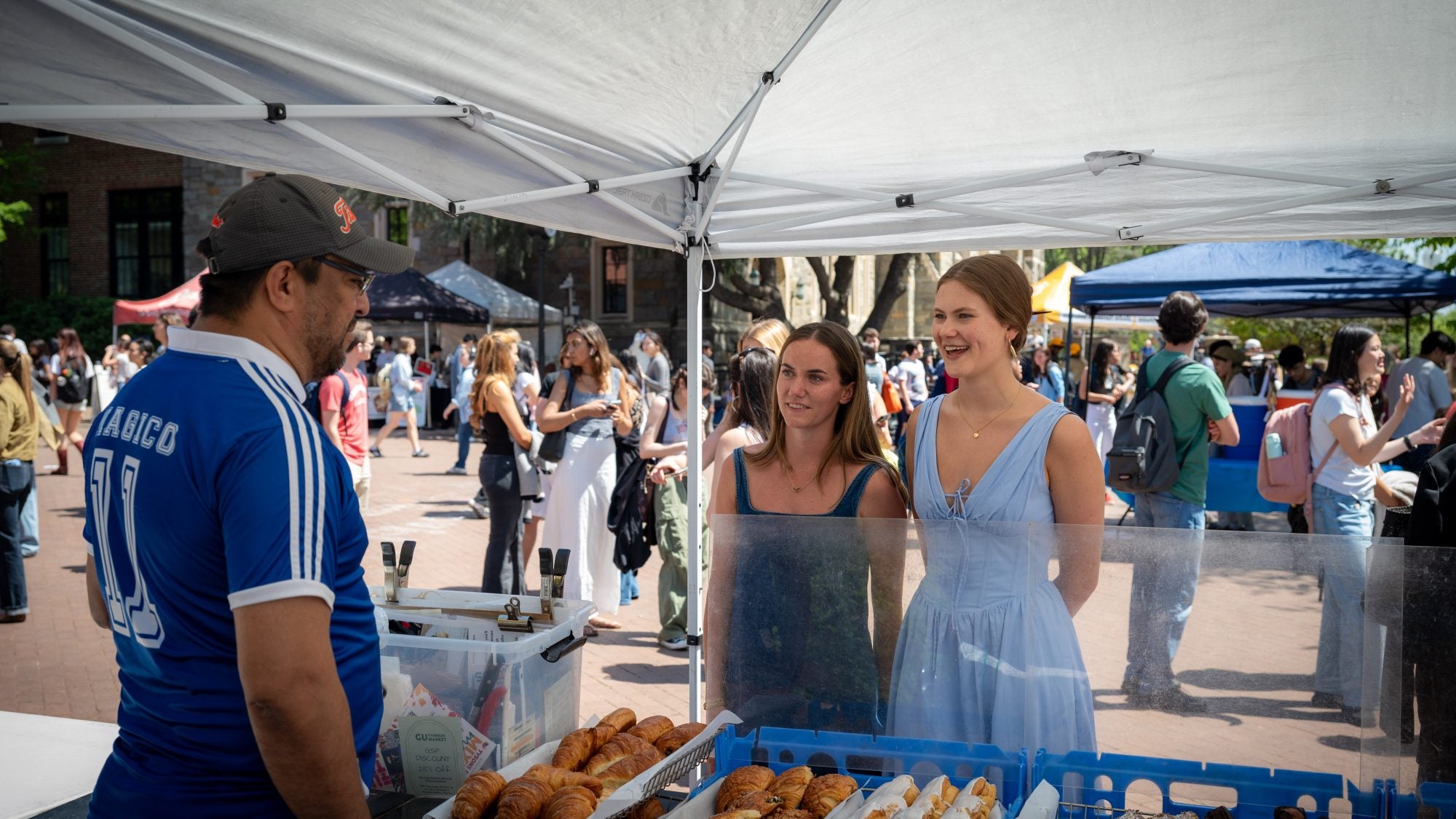 Two young women talk to a man at a pastry stand