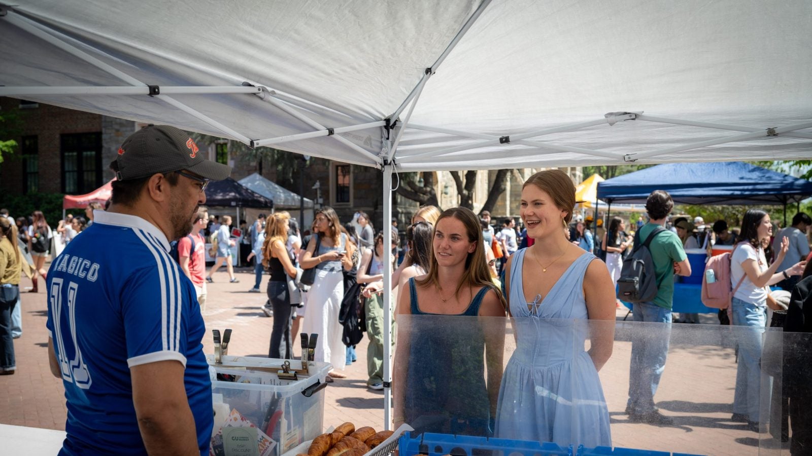 Two young women talk to a man at a pastry stand