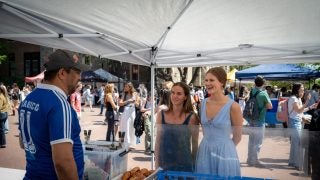 Two young women talk to a man at a pastry stand
