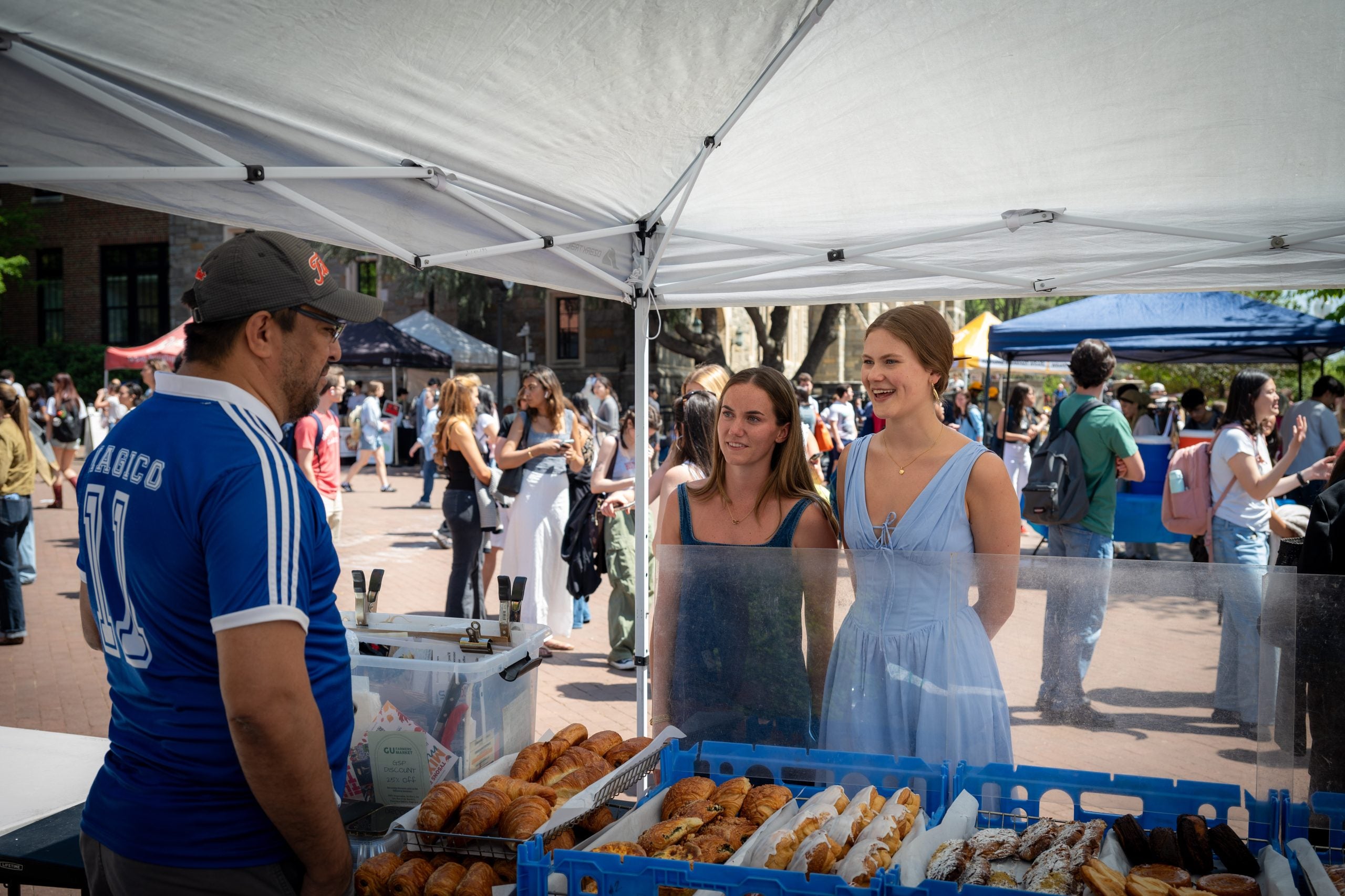 Two young women talk to a man at a pastry stand