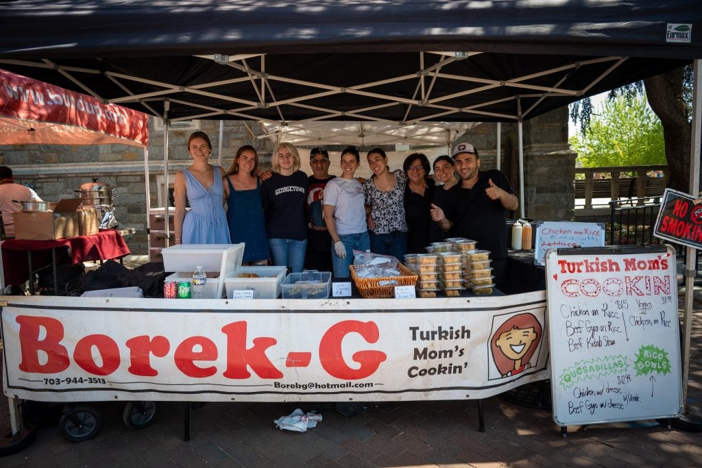 A group of people behind a food stand that says "Borek-G"