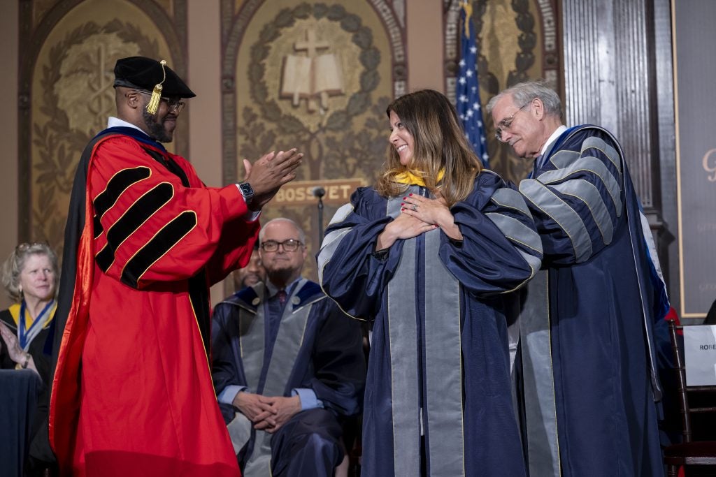 A woman smiles as she receives an honorary degree onstage at commencement