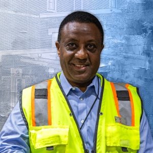 A man wears a blue button down with a yellow vest over it.