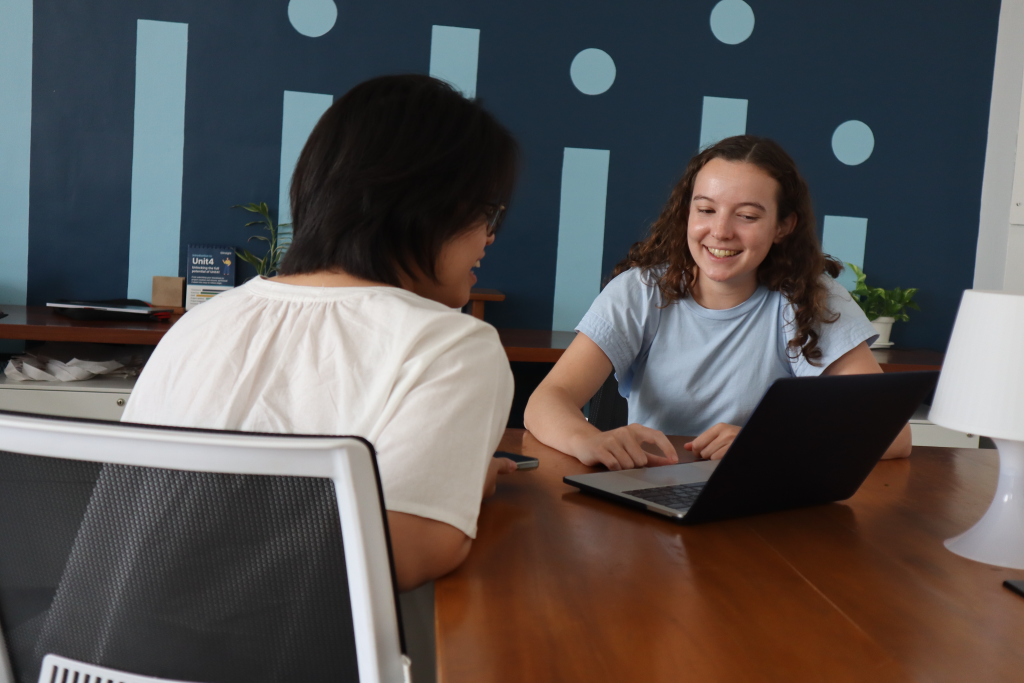 A young woman speaks to another woman while on a laptop