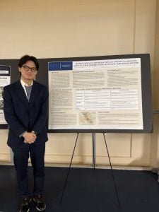 Brian in a suit standing next to a poster board
