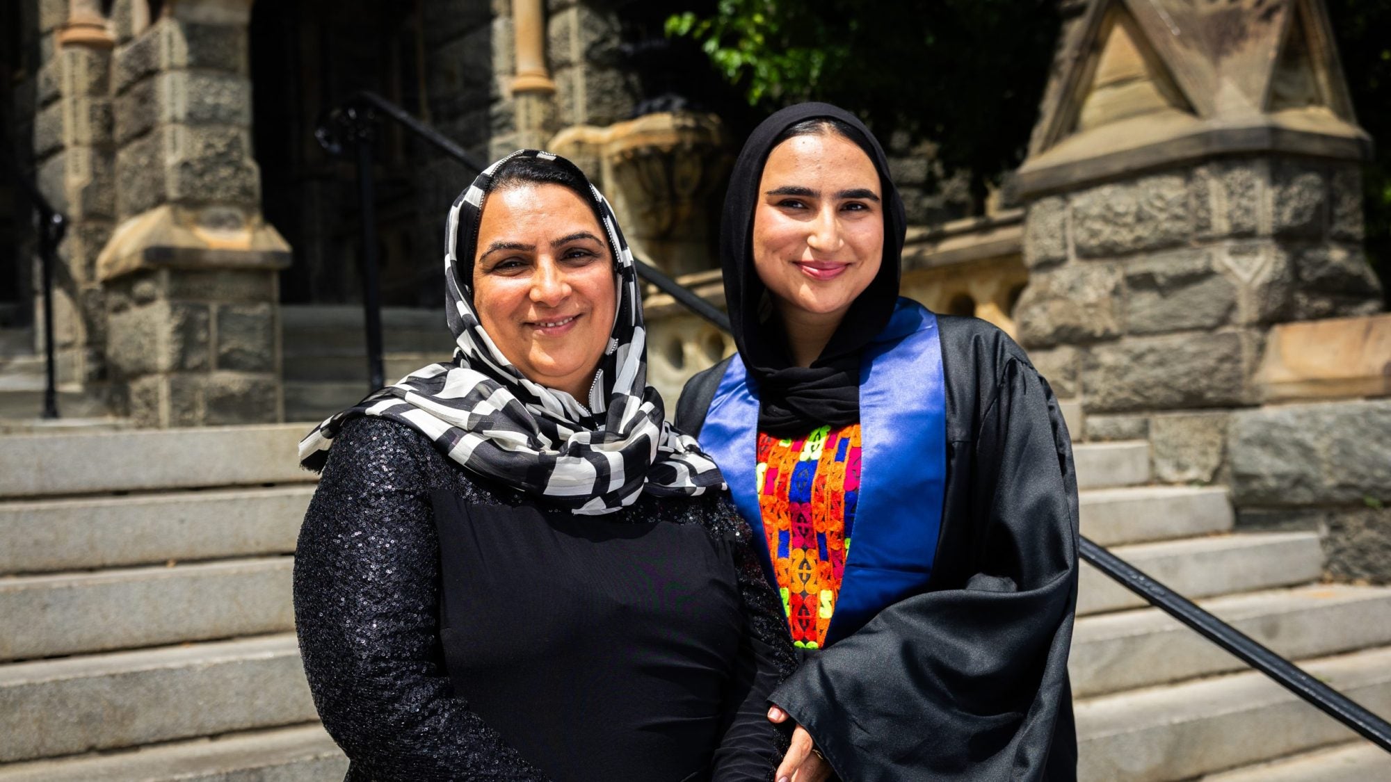 A mother and daughter both wear hijabs and smile on stone steps
