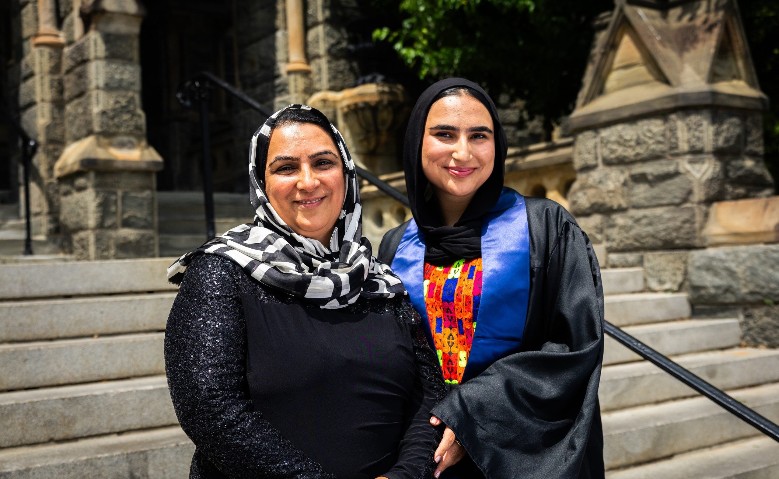 A mother and daughter both wear hijabs and smile on stone steps