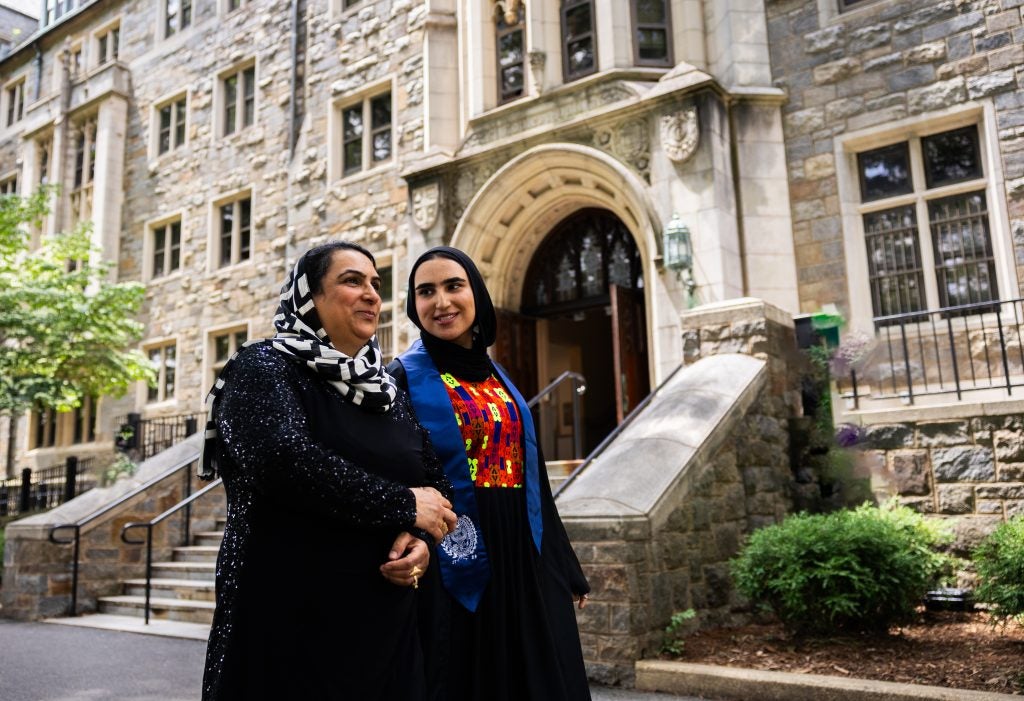 Two women in hijabs walk on Georgetown's campus past a stone building