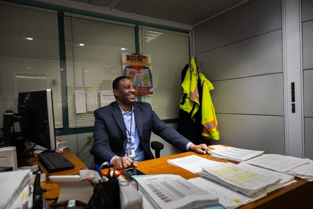 A man in a suit smiles from behind his desk