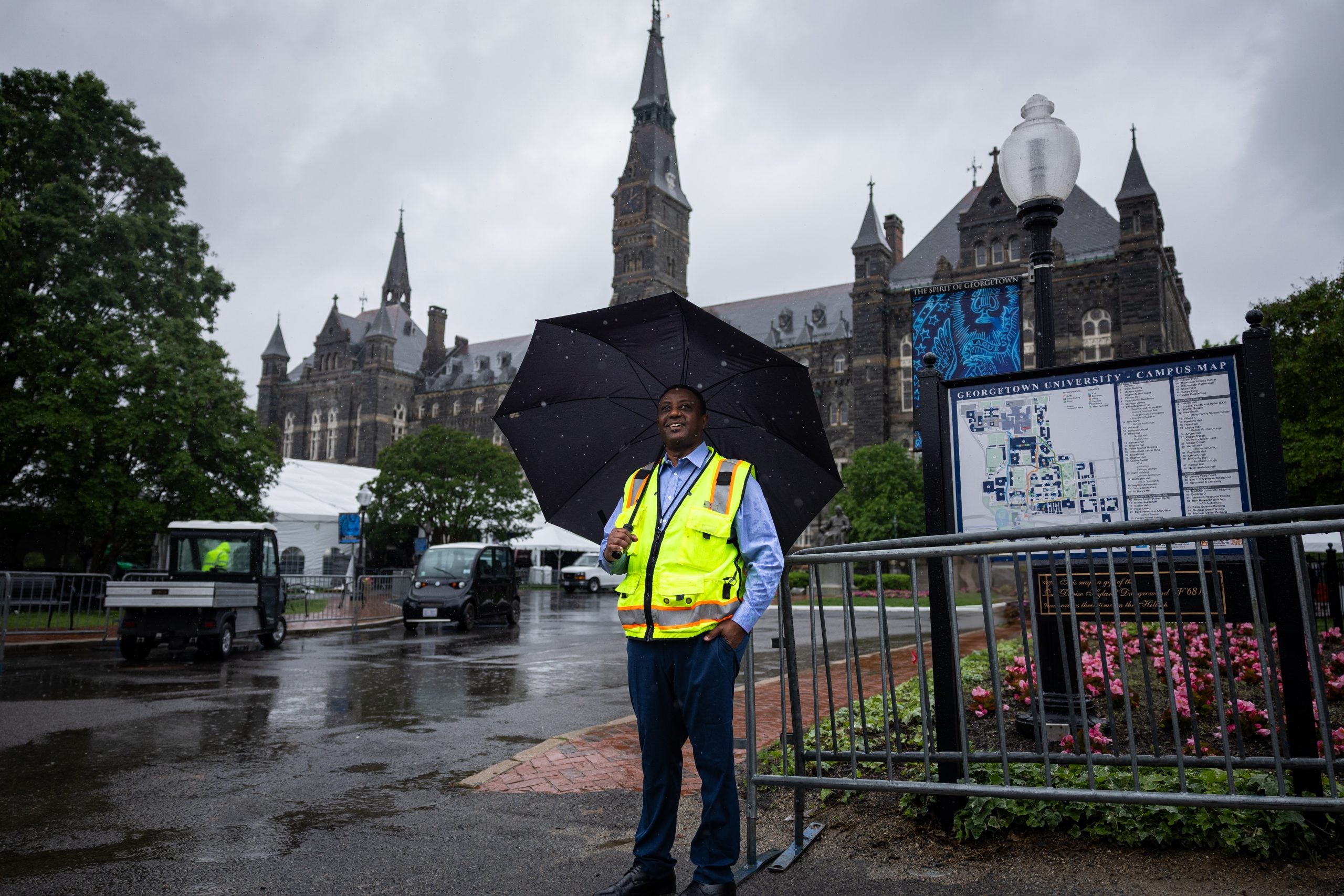 A man in a yellow vest holds an umbrella in front of Healy clocktower on Georgetown's campsu