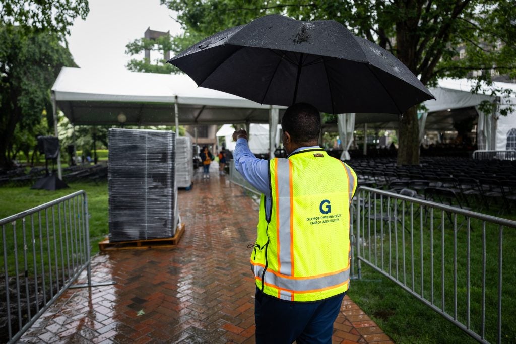 A man in a yellow vest holds an umbrella and walks down a brick pathway in the rain