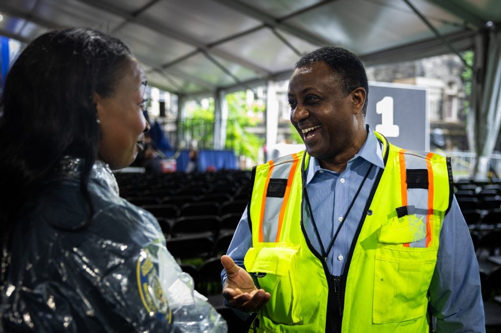 A man in a yellow vest laughs while talking  under a tent