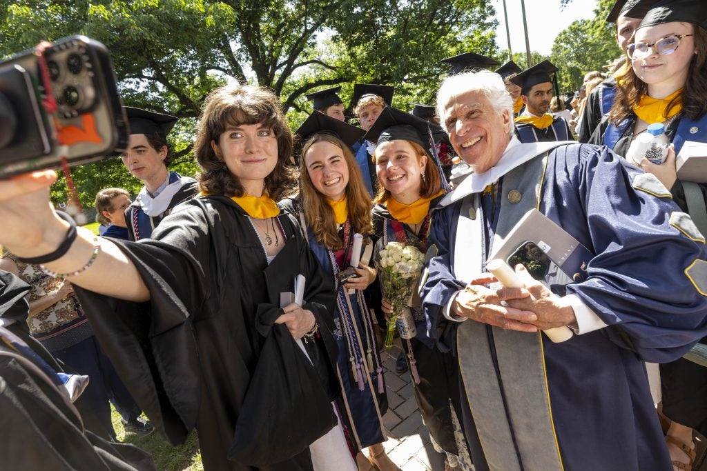 A group of students in graduation gowns take a selfie with Henry Winkler