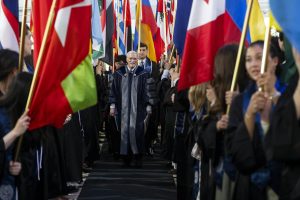 Robert M Groves walks through many flags at convocation