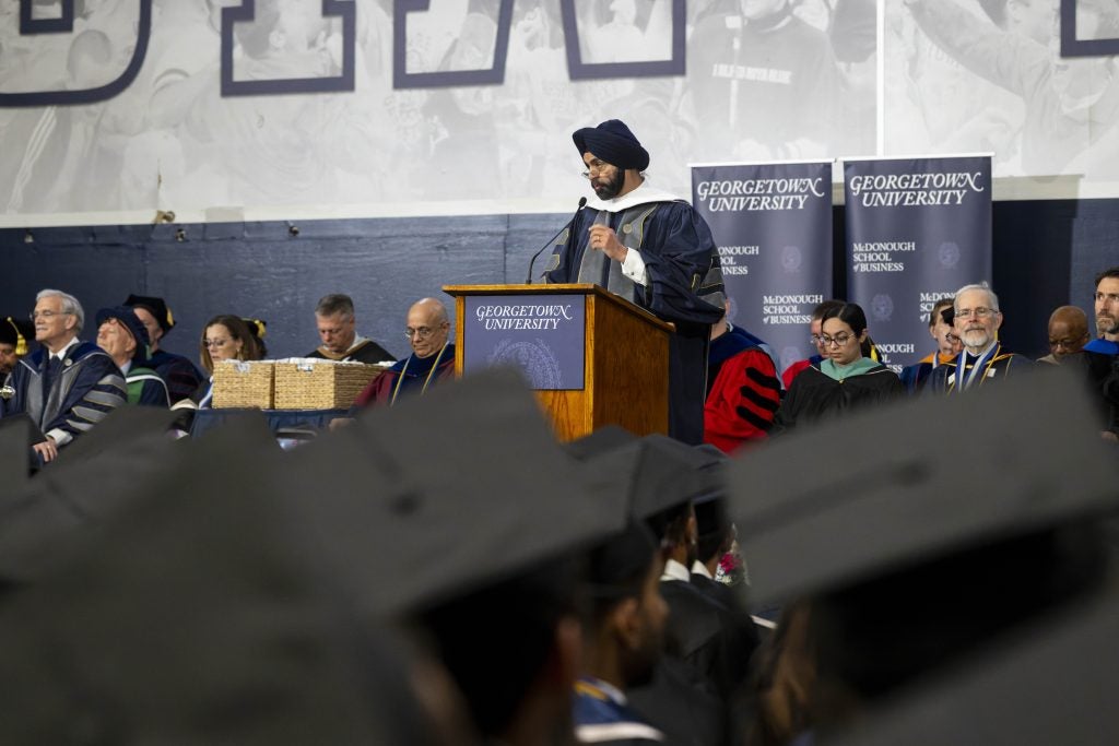 A man in a turban speaks at a podium in a gym