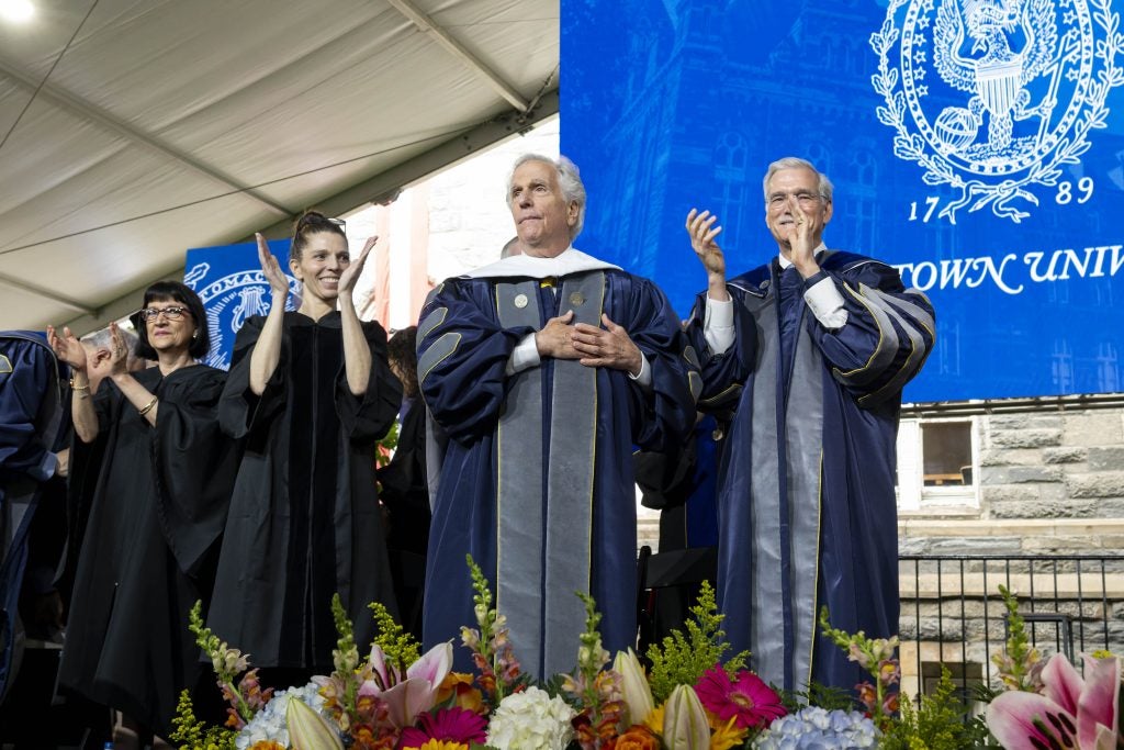 Henry Winkler places his hands over his heart on a stage during graduation