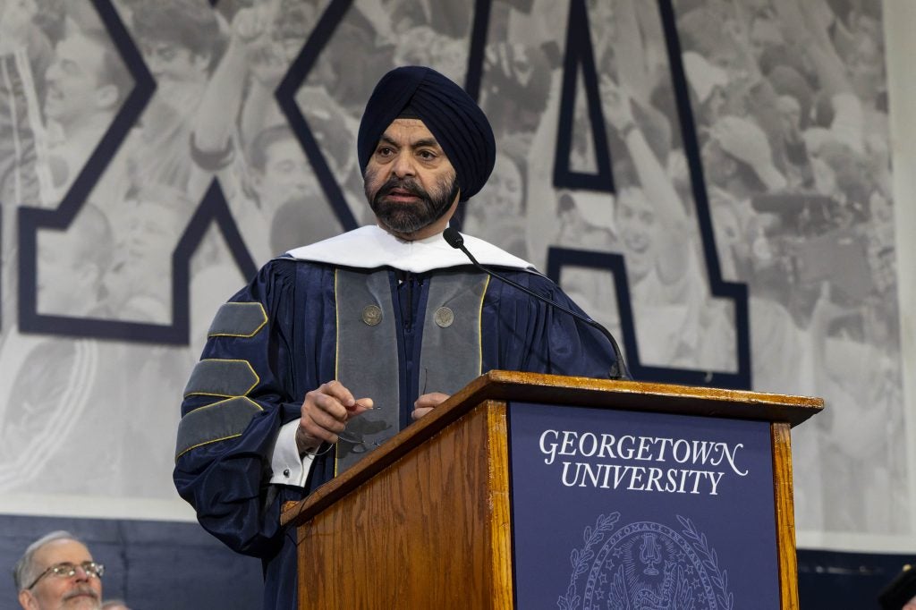 A man in a graduation gown and a turban stands behind a podium