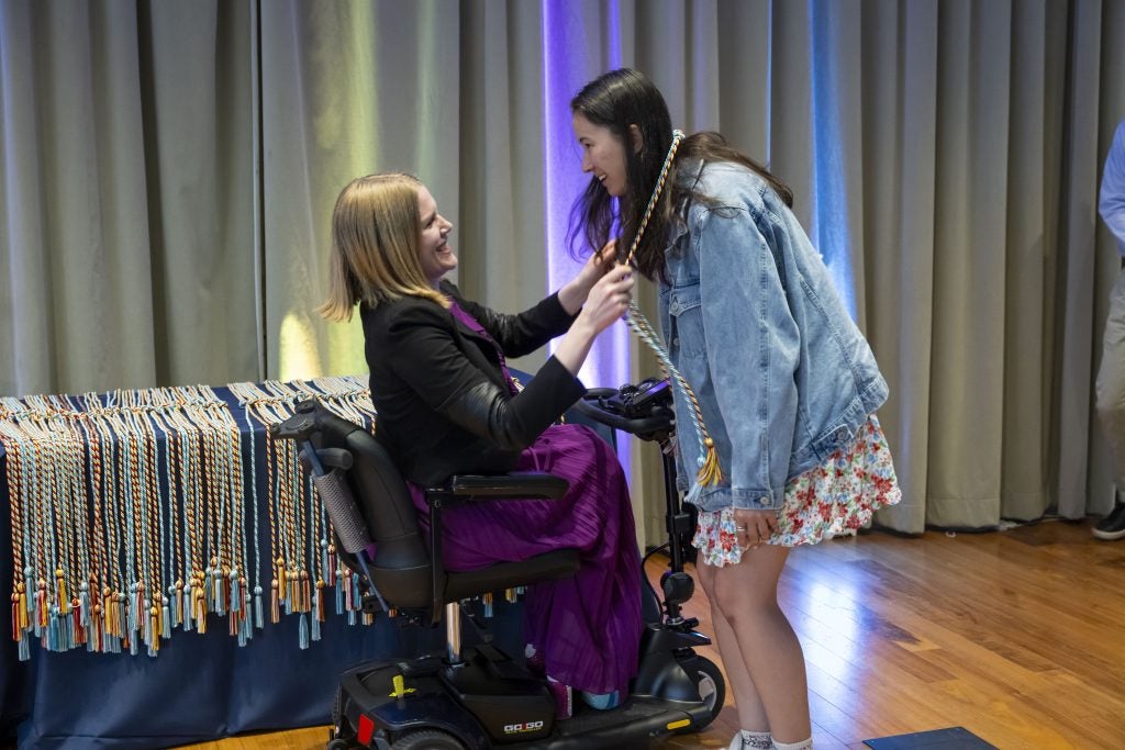 A woman in a wheelchair puts a graduation cord on a student