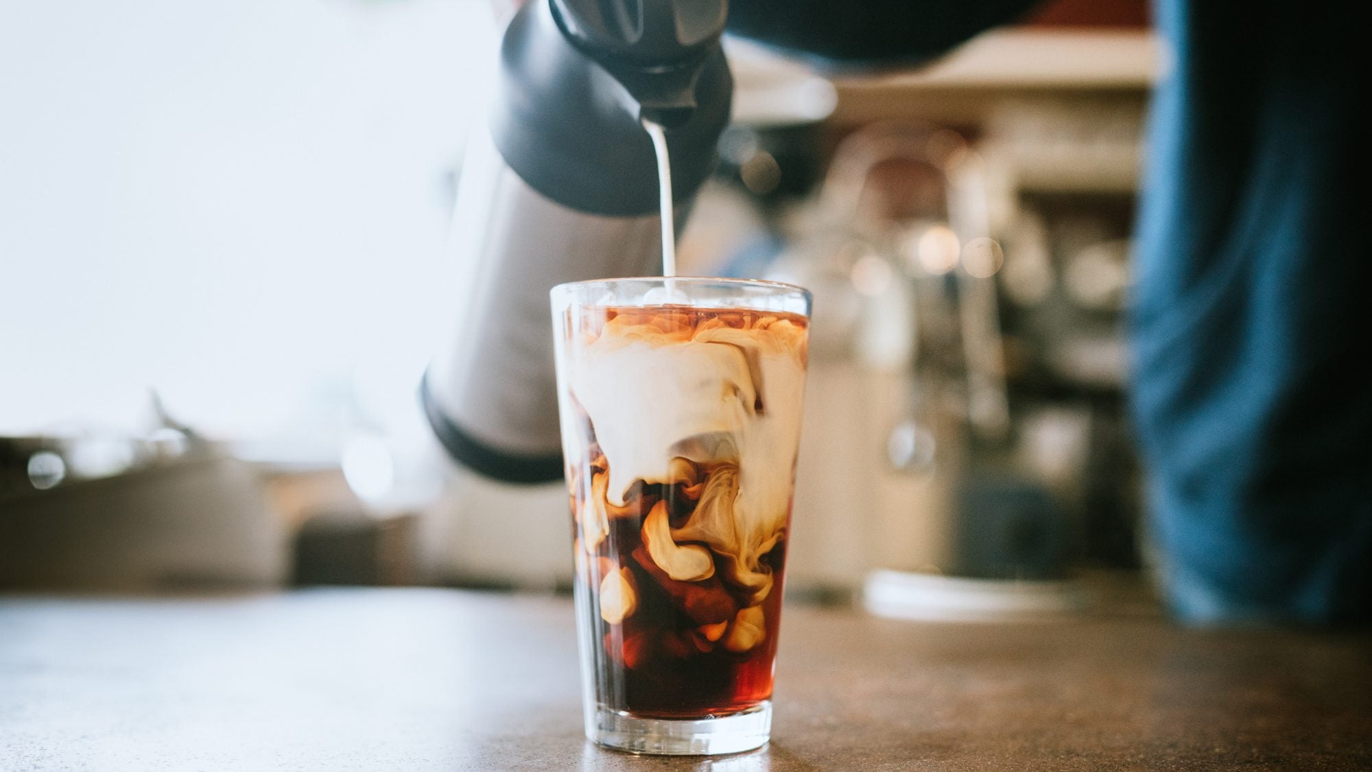 A man pours cold whole milk in to a glass of iced coffee in a cafe. A cool refreshing drink for a hot summer day.