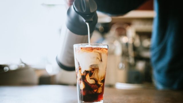 A man pours cold whole milk in to a glass of iced coffee in a cafe. A cool refreshing drink for a hot summer day.