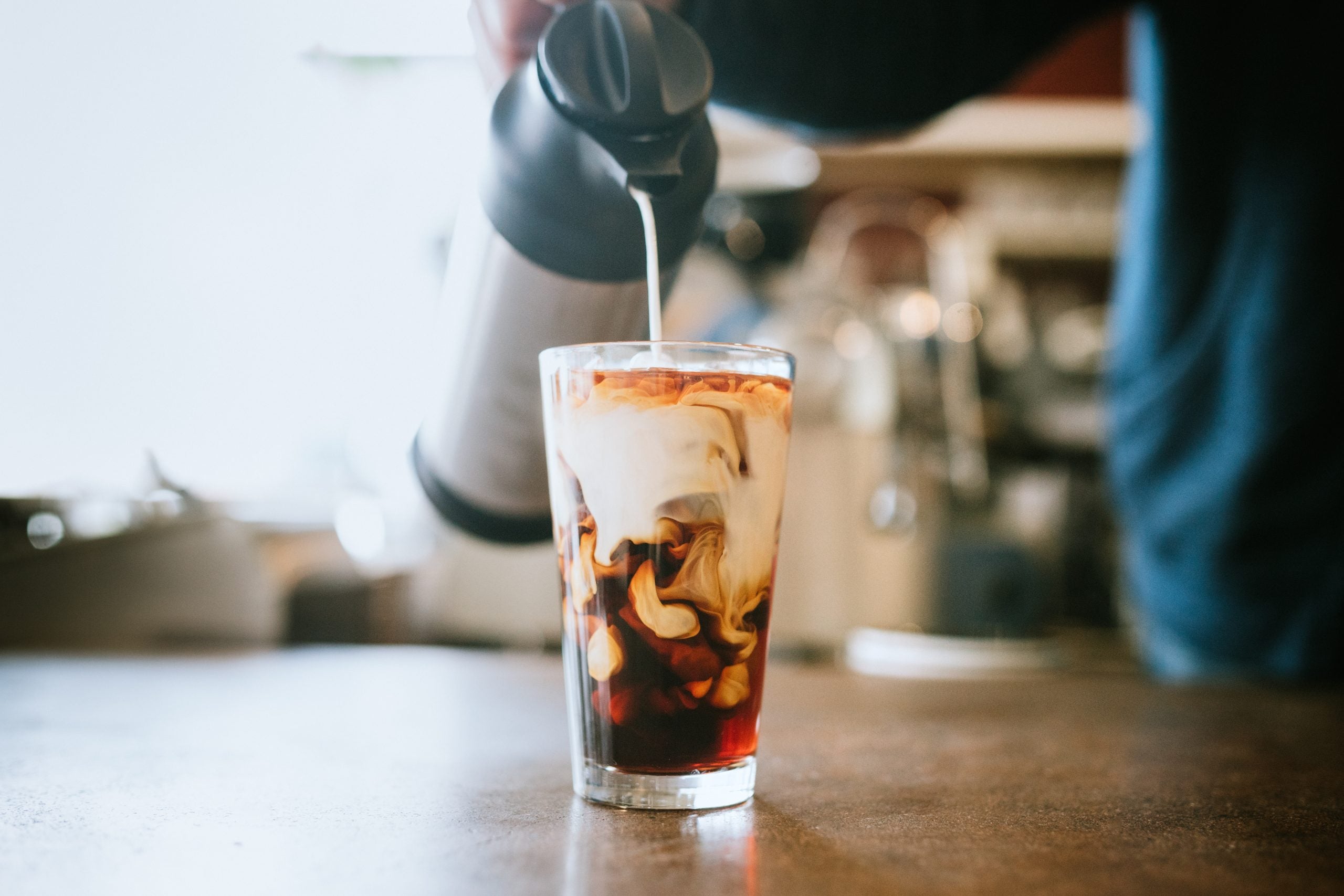 A man pours cold whole milk in to a glass of iced coffee in a cafe. A cool refreshing drink for a hot summer day.