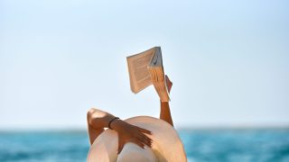 Young woman reads a book on the beach stock photo