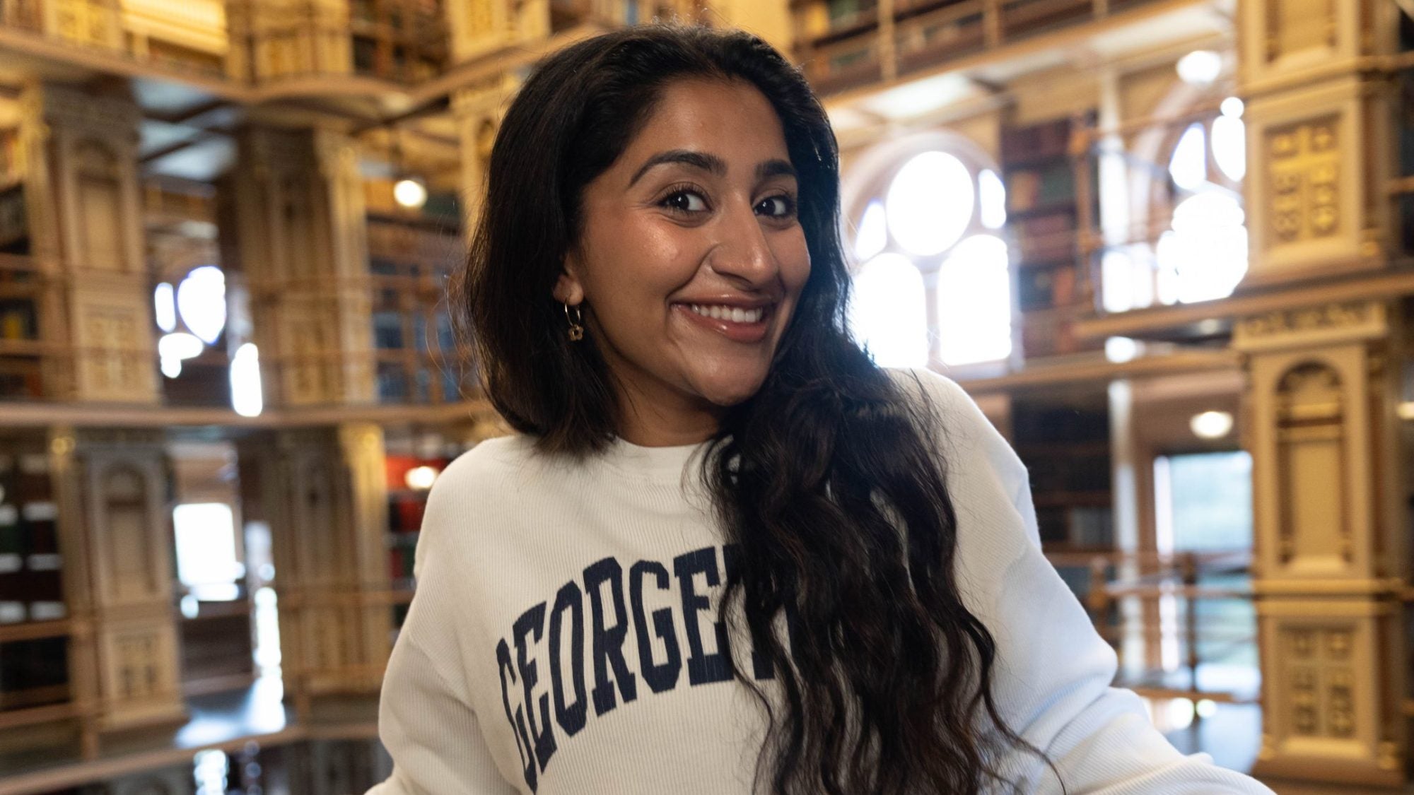 Harnoor in Riggs library in a Georgetown sweatshirt