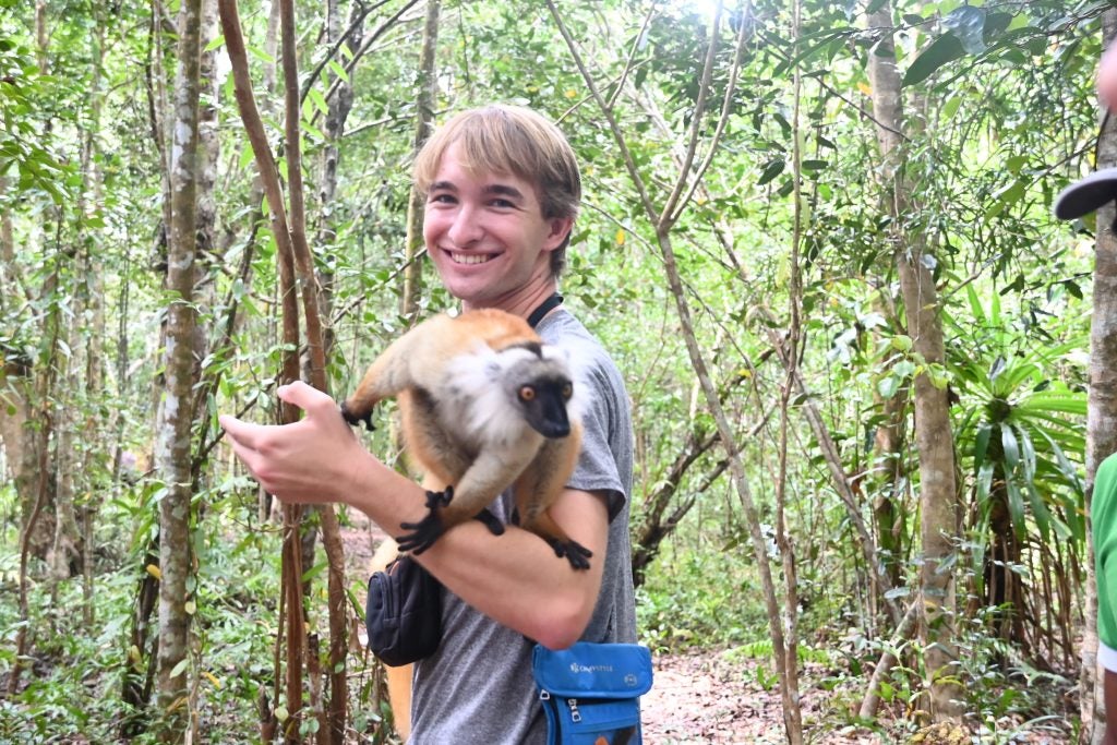 A male student poses with a lemur on his arm in a jungle
