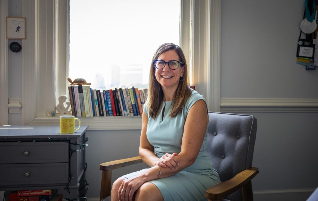 A woman smiles while sitting in front of books perched on a window