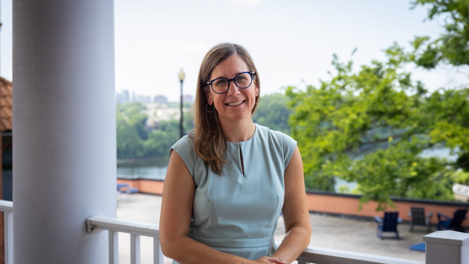 A woman in a light blue dress smiles on a patio overlooking the Potomac River