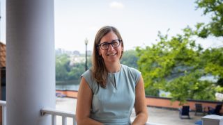 A woman in a light blue dress smiles on a patio overlooking the Potomac River