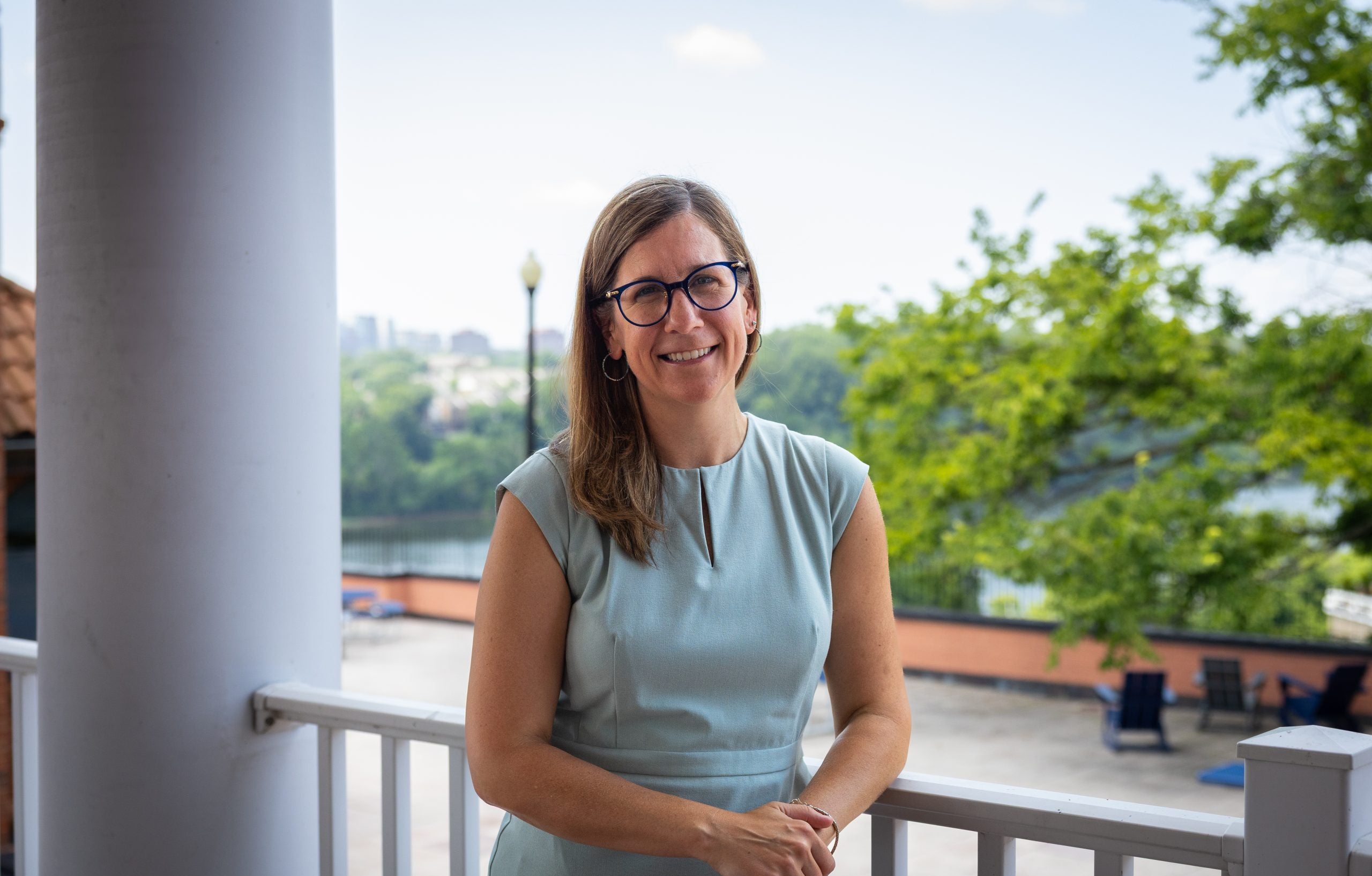 A woman in a light blue dress smiles on a patio overlooking the Potomac River