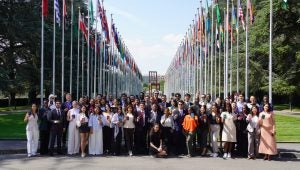 A group of people hold passports at the UN office with flags behind them