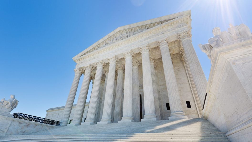 The front of the Supreme Court, with white columns and steps leading up to it, on a sunny day