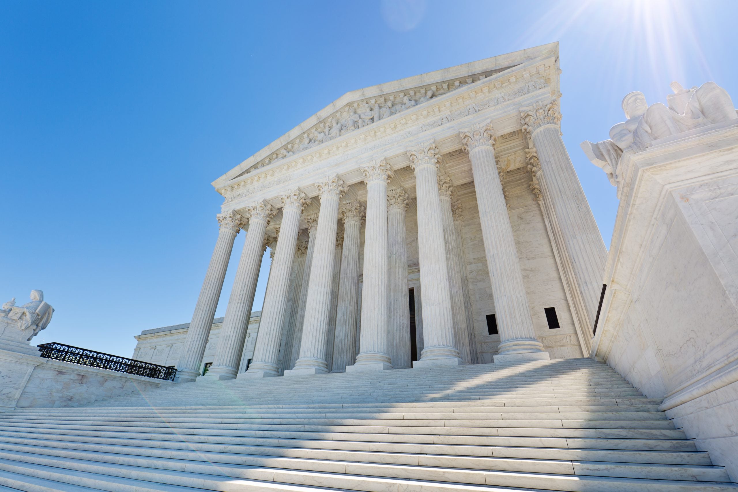 The front of the Supreme Court, with white columns and steps leading up to it, on a sunny day