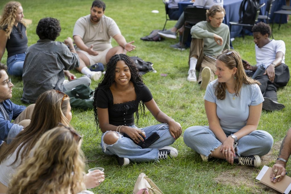 A group of students sit cross-legged in a circle on the lawn