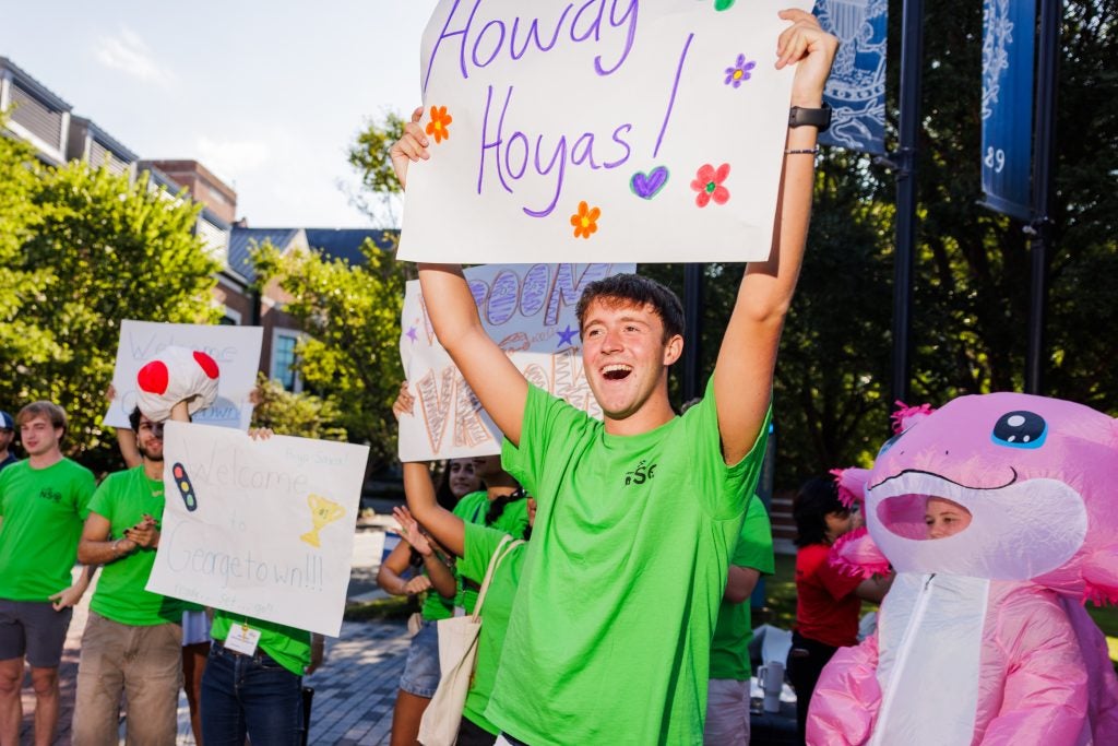 A student smiles as he holds up a sign that says Howdy Hoyas!